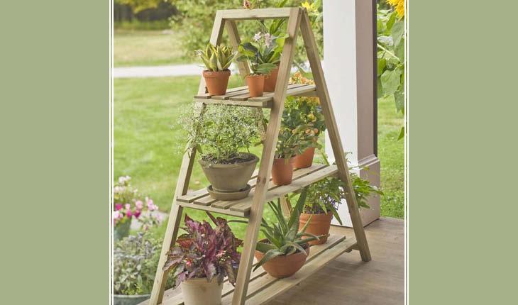 na foto há uma escada de madeira simples aberta e em seus pés estão apoiadas tábuas de madeira. Em cima destas estão vasos de plantas.