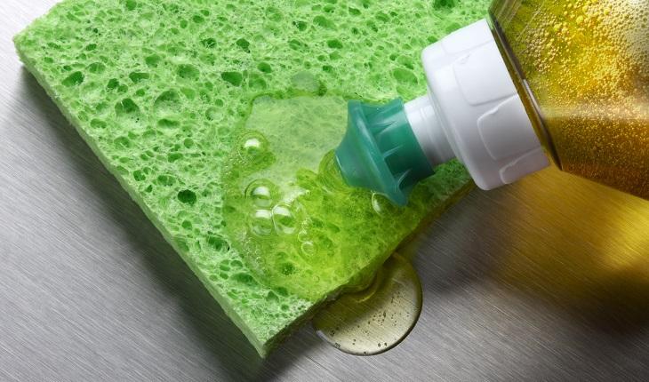 Esponja de cozinha verde com detergente sendo colocado.