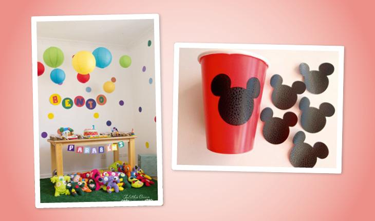 Na imagem há duas fotos de ideias de decoração de festa infantil e o fundo da imagem é rosa-claro. Na primeira foto há uma mesa de madeira com a parede decorada com adesivos de bolinhas e bexigas. A segunda foto mostra como decorar um copo com uma cabeça do Mickey.
