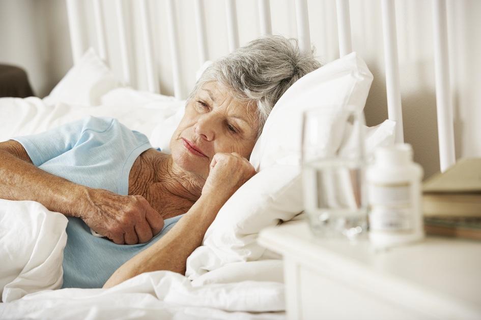 idosa deitada numa cama doente ao lado de remédios