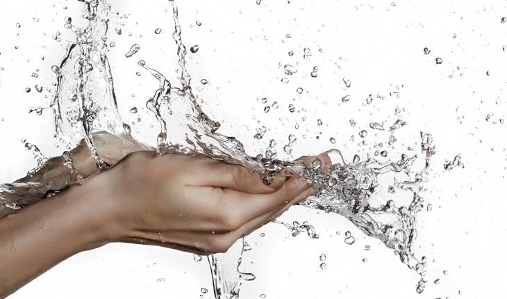 pessoa lavando as mãos com água em abundância. Foto com fundo branco.