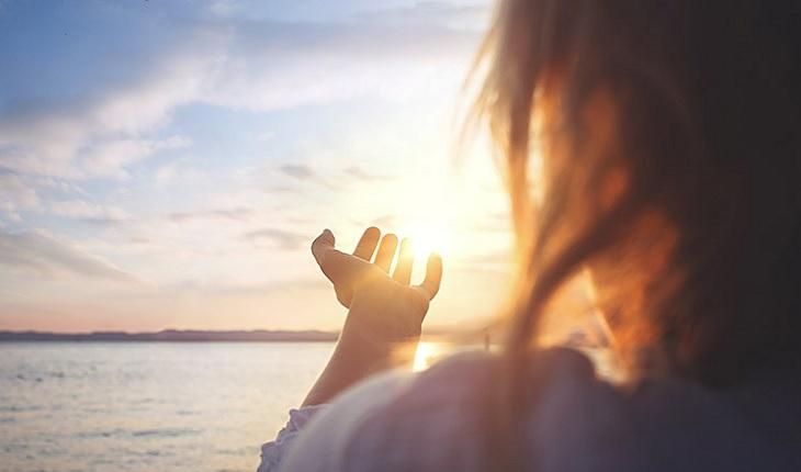A foto mostra uma mulher com as mãos estendidas em direção ao pôr do sol, representando a superação do luto