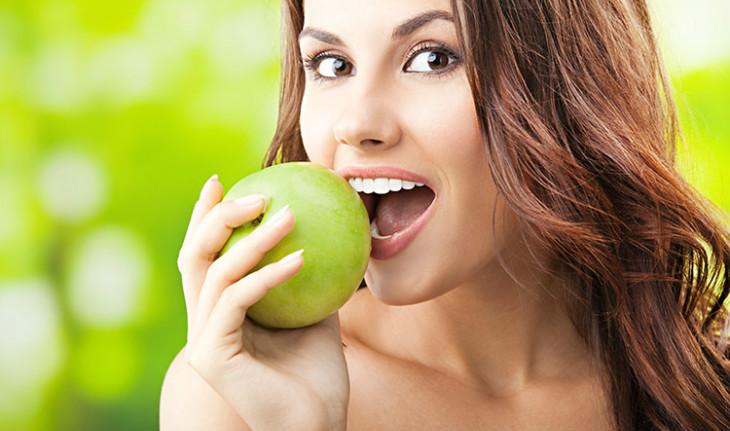 mulher comendo maçã verde, alimento rico em fibra para ficar com a barriga zero