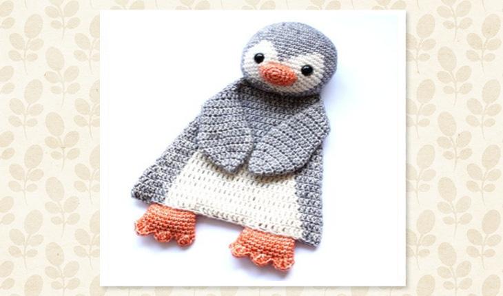 Na foto há uma naninha de crochê de pinguim em que o corpo dele é forma a manta de crochê