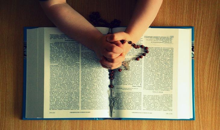imagem de mãos entrelaçadas em sinal de oração segurando um terço. As mãos estão sobrepostas em cima de uma bíblia. orações de proteção para a família