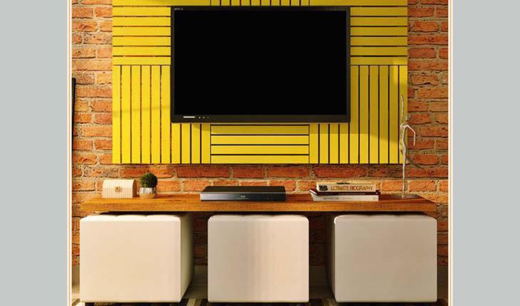 Na foto há um painel de paletes amarelo com uma TV. Embaixo há um aparador.