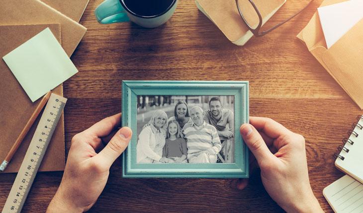 foto de mão segurando um porta retrato com armação azul e foto de uma família