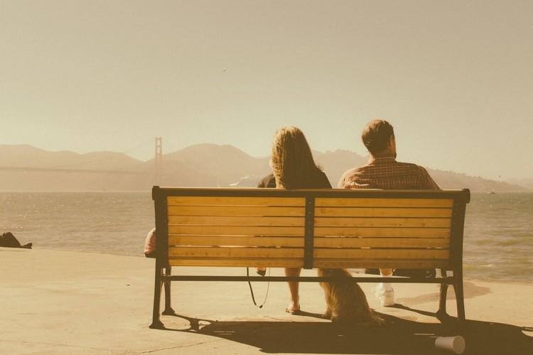 Imagem de um casal sentado em um banco de praça afastados um pouco um do outro. Proteção para o amor e a família