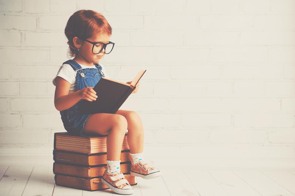 Menino lendo um livro, sentado em uma pilha de livros para ilustrar o tema 5 motivos para ensinar inglês para crianças com autismo