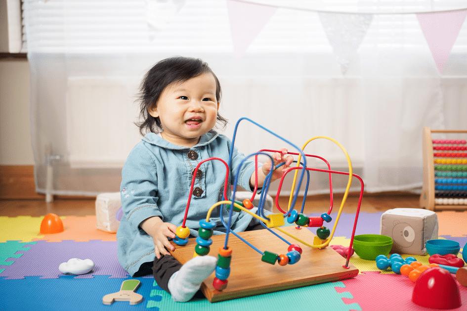 Bebê sentado em um piso colorido e brincando com brinquedo para ilustrar o tema 5 motivos para ensinar inglês para crianças com autismo