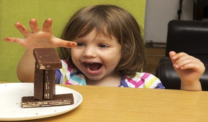 Imagem de uma menina comendo doces em uma mesa - Ana Luíza