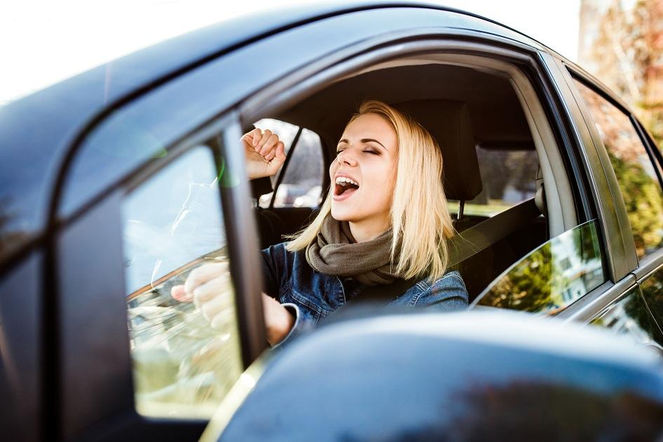 Mulher feliz e leve, cantando enquanto dirige um carro