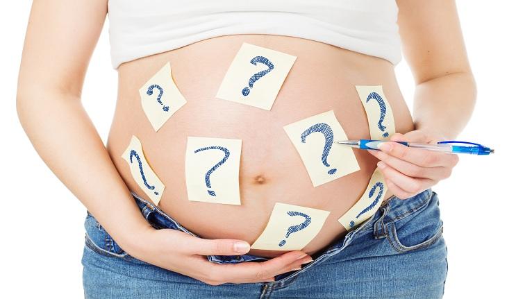 Imagem de uma mulher grávida colocando adesivos com ponto de interrogação em sua barriga. Gravidez.