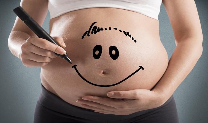 gravidez: imagem de uma mulher grávida desenhando um sorriso com caneta em sua barriga.