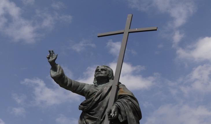 Imagem de um estátua de Jesus Cristo levantando uma cruz sob um dia ensolarado. Amor protegido