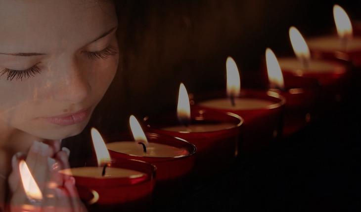 Imagem de uma mulher ao lado de velas realizando uma oração. Amor protegido