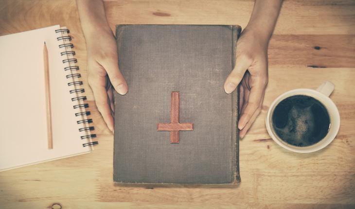 biblia, cafe e caderno com lapis em cima da mesa. Uma mulher segura a biblia com as duas maos