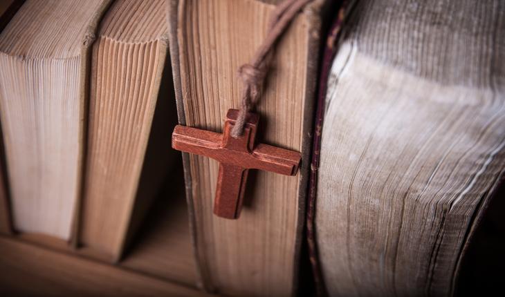 biblias em uma estante com um cordao com uma cruz apoiado sobre uma delas
