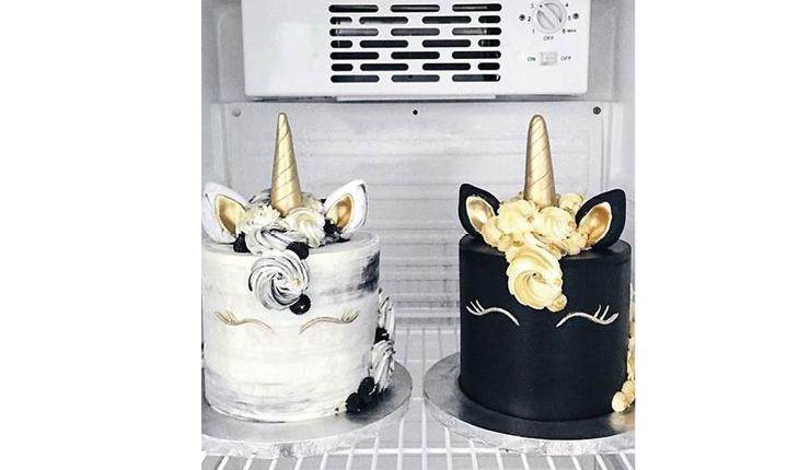 Na foto há dois bolos redondos que formam o rosto dos unicórnios. Um deles é é branco com acabamento em mármore e o outro é preto. Os detalhes são feitos em dourado, assim como os chifres. O rosto é feito apenas do os olhos fechados do unicórnio.