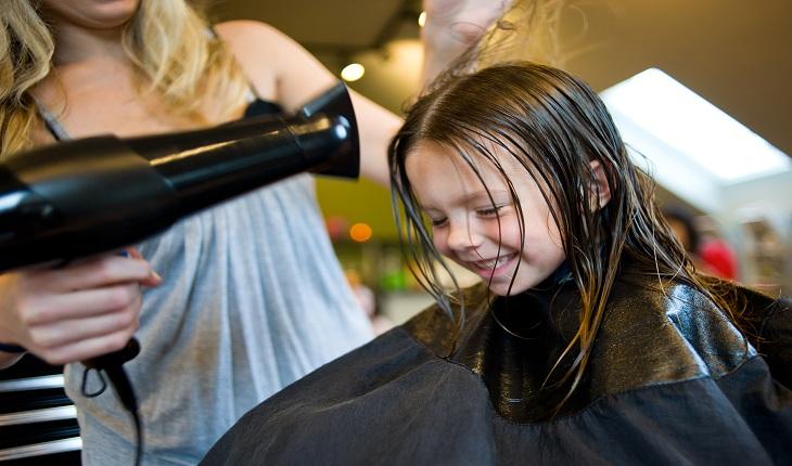 Menininha sorridente cortando o cabelo no salão de beleza