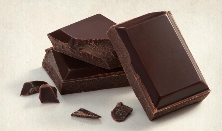 Foto com pedaços de chocolate amargo que compõe uma lista com os alimentos que dão sensação de bem-estar e tranquilidade.