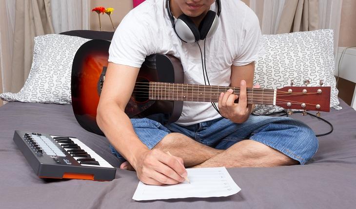Homem compositor segurando violão e escrevendo em um papel