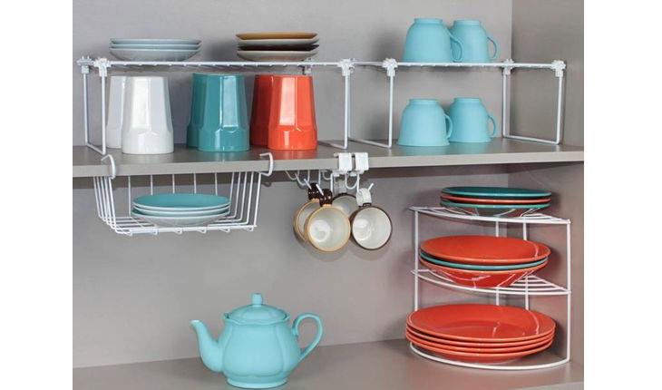 A foto mostra um suporte de metal que serve como armário. O suporte tem espaço para copos, pratos, xícaras, entre outros utensílios, que ficam à vista. As louças da foto são nas cores azul e vermelho.
