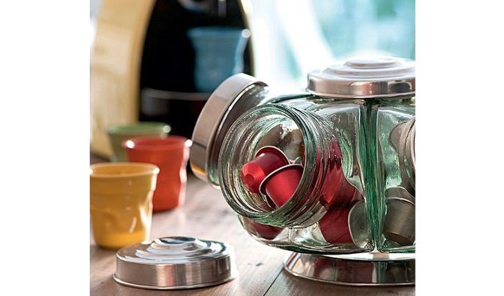 A foto mostra uma baleiro de vidro sendo utilizado para organizar outros itens de cozinha. No caso da foto, está organizando cápsulas de café.
