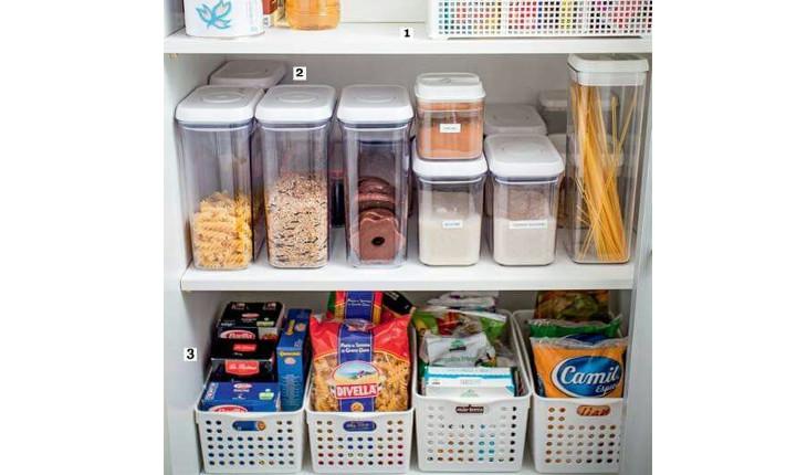 A foto mostra uma estante de comida em que todos os alimentos estão divididos em potes transparentes ou organizados em cestos de plástico firme e branco.