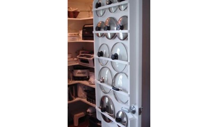 A foto mostra um suporte que fica em uma porta de um armário de cozinha. O suporte serve para guardar tampas de panelas.