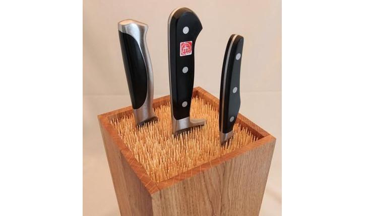 A foto mostra um suporte alto de madeira com palitos de madeira dentro. As facas ficam espetadas dentro do bloco, nos palitos.