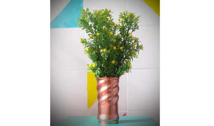 Na foto há uma lata de achocolatado pintada na cor cobre que tem uma planta dentro.