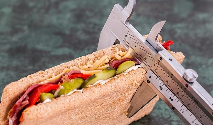 Na imagem, um sanduíche saudável está sendo medido com uma régua especial para medir gordura no corpo. Anticoncepcional oral.