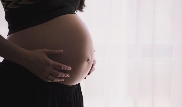 Na imagem, uma barriga de uma mulher grávida está em foco. Anticoncepcional oral.