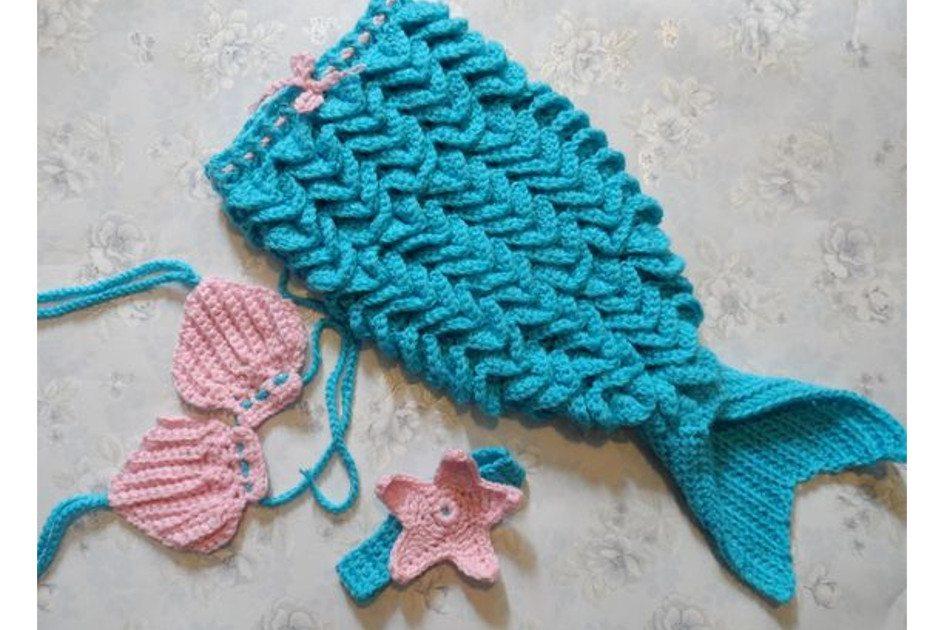 Na foto há uma fantasia de crochê para bebê de sereia. A calda é azul e a parte de cima é um biquíni rosa e azul.