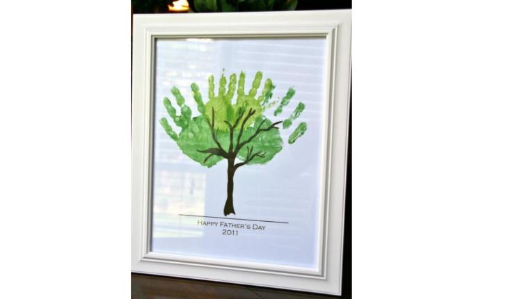Na foto há um quadro branco com o desenho de uma árvore em que o topo da árvore é feito com o carimbo das mãos de crianças.