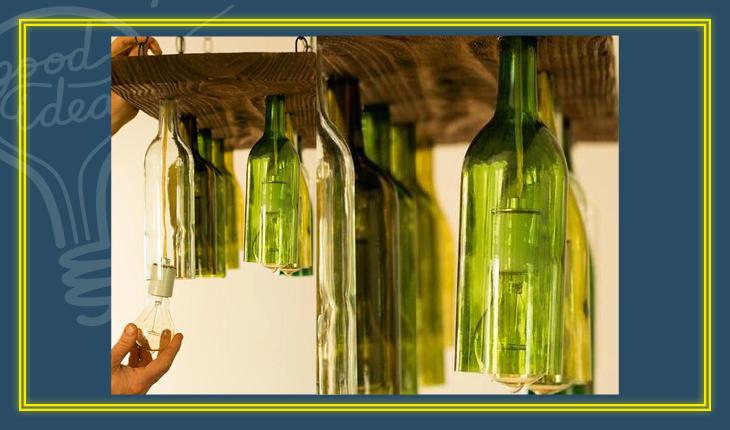 Na foto há várias garrafas de vidro verdes em um suporte de madeira que serão utilizadas como luminárias.