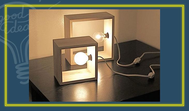 Na foto há duas luminárias de mesa feitas com quadrados de concreto, com as lâmpadas fixas em um dos lados do quadrado.