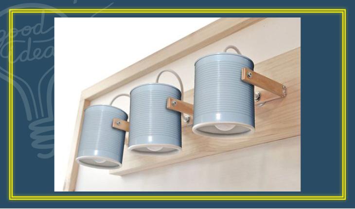 Na foto há três latas de aço pintadas de azul em um suporte de madeira formando um luminária de foco.