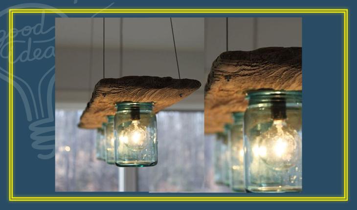Na foto há uma luminária feita com copos de vidro verdes que estão em um suporte de madeira. As lâmpadas estão dentro de cada um dos copos.