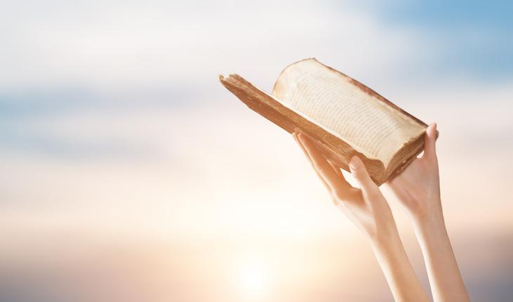 maos segurando uma biblia aberta em diração do céu