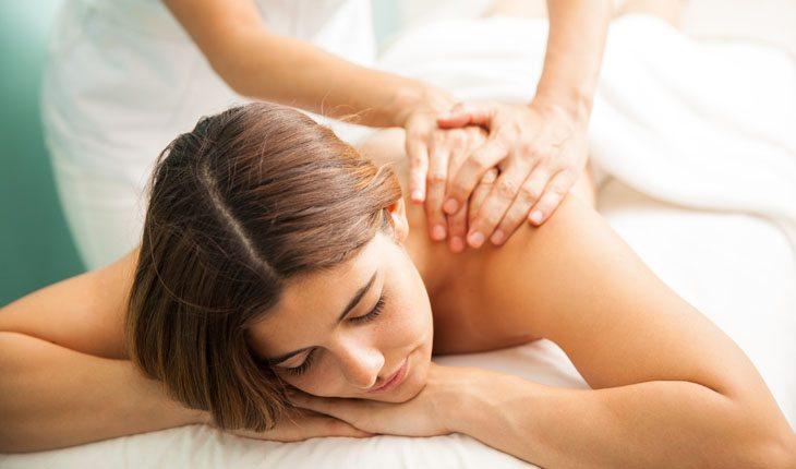 mulher deitada de bruços recebendo massagem nos ombros
