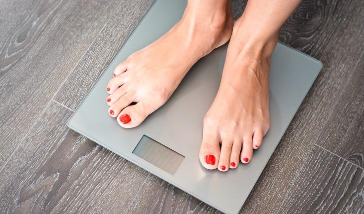 mulher sobre uma balança se pesando. Um dos motivos para inserir a batata-doce na dieta é a perda de peso.