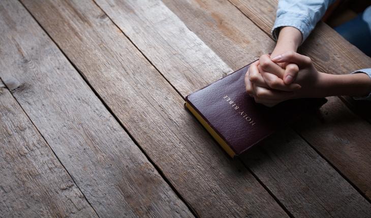 mulhersentada comasmaos em posicao de oracao apoiadas sobre uma biblia