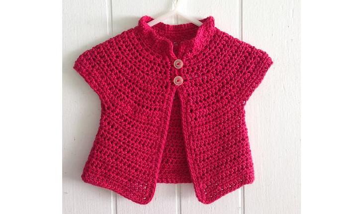 Na foto há um casaquinho de bebê feito de crochê nas cores rosa-escuro.