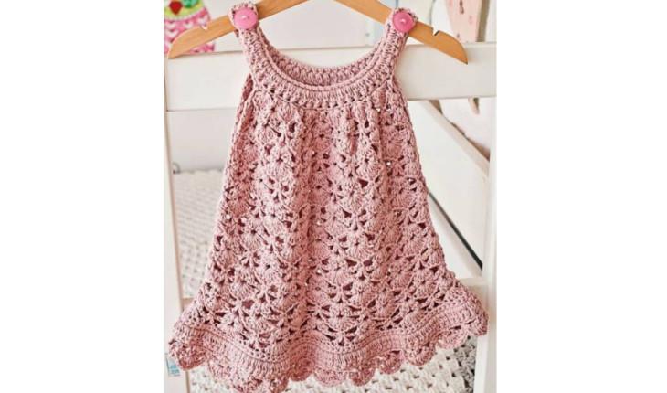 Na foto há um vestidinho de alça para bebê feito de crochê. Sua cor é rosa.