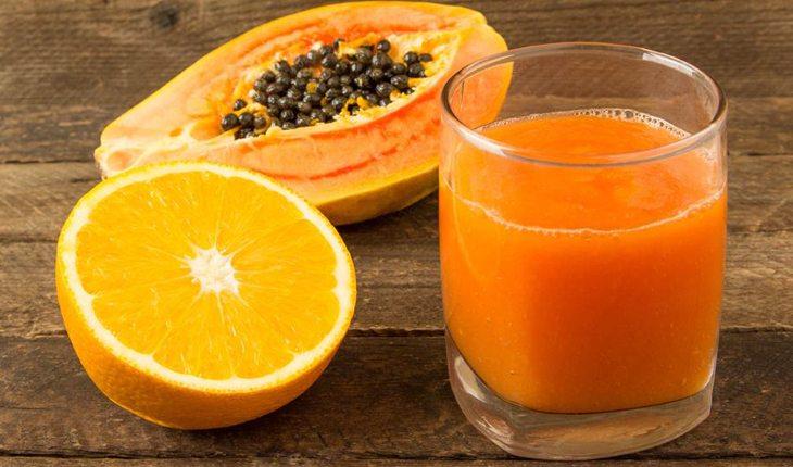 suco de laranja, mamão, maçã e morango servido em um copo de vidro, com meia laranja e meio mamão decorando