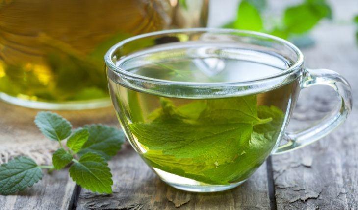 xícara de chá verde com folhas dentro