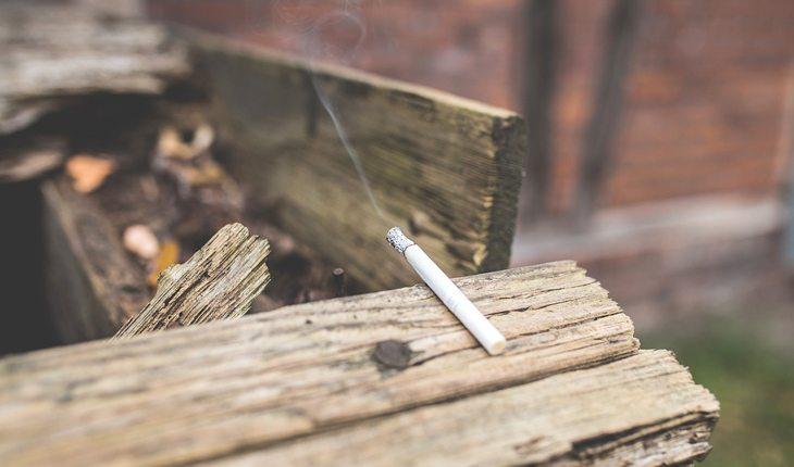 Foto de um cigarro aceso em cima de um pedaço de madeira