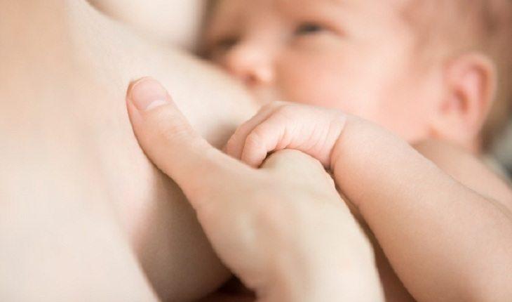 Na imagem, o bebê está sugando leite do peito enquanto encosta a mão no dedo da mãe. Dispositivo intrauterino.